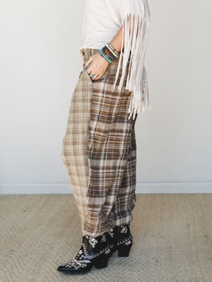 A side-profile shot of a relaxed plaid wide-leg trouser paired with a cream fringe top and embroidered black cowboy boots — the kind of outfit that makes you look like you know exactly who you are.