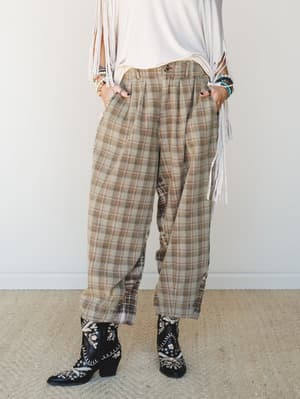Relaxed plaid trousers in warm tan and brown tones styled with a cream fringe top and embroidered black cowboy boots — the kind of outfit that looks effortlessly pulled together without trying too hard.