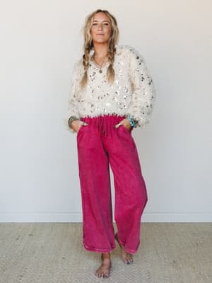 A relaxed, playful outfit pairing — a cream sequin fuzzy sweater with wide-leg raspberry-washed pants, styled with stacked boho jewelry and loose braids for that effortlessly put-together feel.