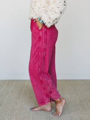 A side-profile shot of relaxed wide-leg pants in washed burgundy paired with a cream sequin fringe top, styled barefoot with turquoise stone bracelets — the kind of outfit that looks equally at home on a couch or at a backyard dinner.