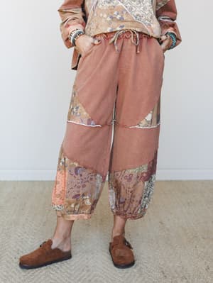 A cropped wide-leg patchwork pant in washed terracotta pairs with a floral tapestry top and rust jacket, styled with suede clogs and stacked bracelets for a lived-in boho look that feels effortlessly collected.