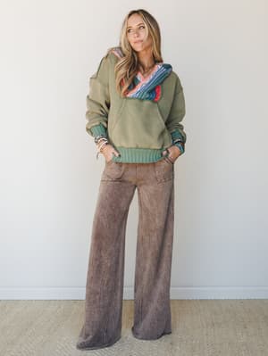 An effortlessly cool outfit combo — an olive hoodie with a multicolor knit hood detail paired with wide-leg mineral-washed pants, styled with stacked bead bracelets for that lived-in boho feel.