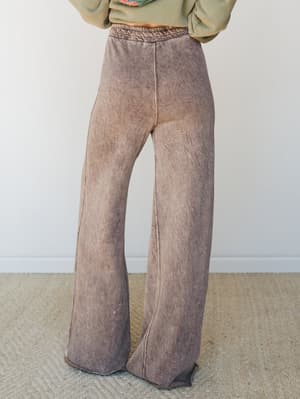 A mineral-washed wide-leg fleece pant in a worn-in mocha tone, shot from the back against a clean studio wall — the kind of pants you wear when comfort is non-negotiable but you still want to look like you meant it.