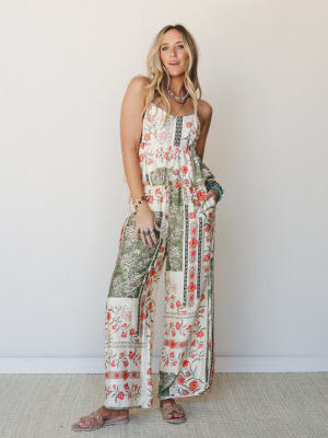 A wide-leg floral print jumpsuit or coordinated set in cream and sage, styled with layered turquoise jewelry and slide sandals — effortlessly boho and made for somewhere warm.