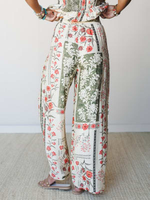 A back-facing shot of wide-leg floral pants in a block-print ecru base, styled with a matching printed smocked top and stacked boho jewelry — the kind of outfit that looks effortless but was definitely thought about.