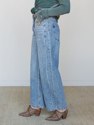A side-profile shot of wide-leg light wash jeans styled with a knotted sage green thermal top, leopard print booties, and turquoise rings — the kind of effortless everyday outfit that somehow always looks intentional.