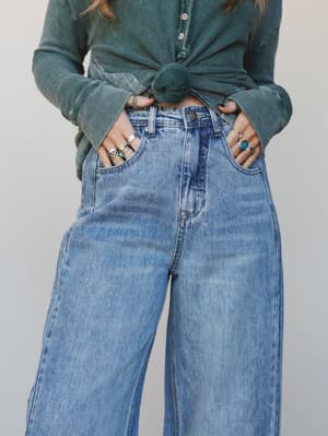 A close-up mid-shot of wide-leg light wash jeans styled with a forest green knotted thermal henley, hands tucked into pockets and stacked silver rings doing a lot of the heavy lifting — effortlessly lived-in and very much the kind of outfit you wear