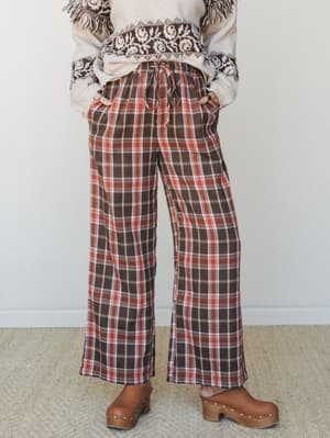 Wide-leg plaid pants in a warm brown and rust colorway, styled with a fair isle fringe sweater and wooden clogs — the kind of autumn outfit that makes you want to walk through leaves and then sit by a fire.