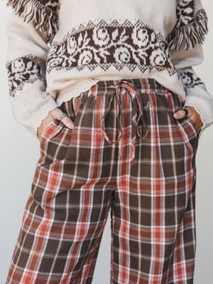 A cozy mid-shot pairing of plaid wide-leg pants with a cream fair isle sweater — the kind of outfit that makes staying in feel completely intentional.