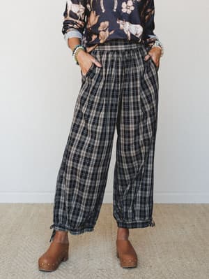 Wide-leg plaid joggers in a moody navy and cream plaid styled with a graphic floral sweatshirt, stacked bead bracelets, and wood-studded clogs — the kind of outfit that looks effortless but is doing a lot of heavy lifting.