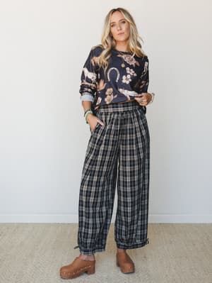 A relaxed, effortlessly collected outfit built around wide-leg plaid joggers paired with a novelty western-print sweatshirt and tan clogs — the kind of look that makes a Saturday coffee run feel intentional.