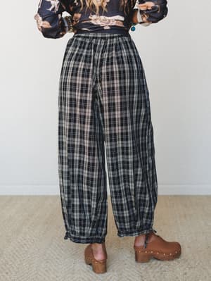 A back-facing shot of relaxed plaid joggers in black and cream, styled with a floral print top and wood-soled clogs — the kind of outfit that feels pulled-together without trying too hard.