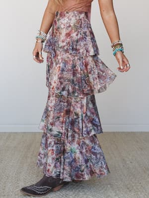 A flowy tiered maxi skirt in a moody floral print styled with cowboy boots and stacked beaded bracelets — the kind of outfit that feels like it was made for wandering somewhere beautiful.