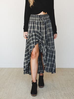 A flowy plaid maxi skirt with a front ruffle slit is styled with a cropped black long-sleeve and ankle boots — the kind of outfit that looks effortless but definitely took two tries.