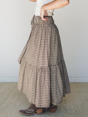 A tiered plaid maxi skirt in warm chocolate and cream tones styled with a white tee and brown cowboy boots — the kind of outfit that makes a Tuesday feel like a road trip.