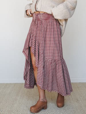 A tiered plaid midi skirt in deep cranberry and cream is styled with an oversized cream knit sweater and tan studded clogs — the kind of fall outfit that feels pulled-together without trying too hard.