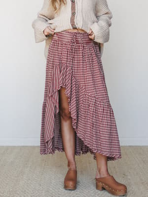 A plaid high-low midi skirt in deep red and cream is styled with a chunky oatmeal cardigan and tan wooden clogs — the kind of effortless fall outfit you'd reach for on repeat.