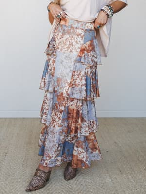 A flowy tiered maxi skirt in a faded floral patchwork print — dusty blue, rust, and cream — styled with a cream tee, stacked turquoise jewelry, and leopard mules for that perfectly effortless boho mix.
