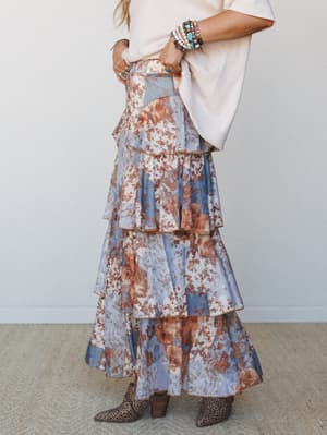 A flowy tiered maxi skirt in a soft periwinkle and rust floral print, styled with a relaxed cream tee, stacked turquoise and silver bracelets, and leopard ankle boots — the kind of outfit that looks effortless but was absolutely thought about.