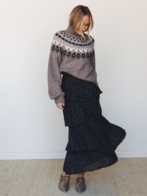 A cozy-meets-romantic fall outfit — a fair isle turtleneck sweater layered over a tiered floral maxi skirt with movement, finished with leopard print mules and stacked rings.