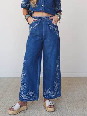Wide-leg embroidered denim pants styled as a matching set with a cropped denim shirt, layered bracelets, and espadrille platform sandals — the kind of outfit that looks effortless but definitely took a minute.