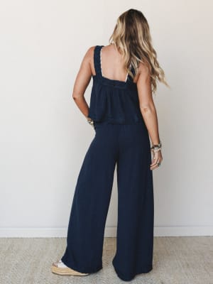 Shot from behind, a model in a deep navy matching set — a flowy crochet-trimmed cami top and wide-leg pants — paired with espadrille wedges and a stack of boho bracelets, giving off easy, effortless summer energy.