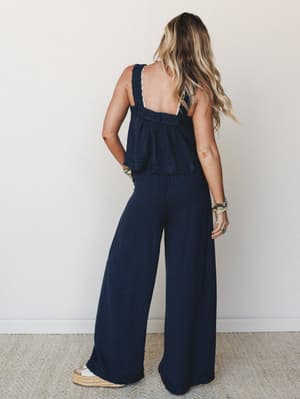 Shot from behind, a model in a deep navy matching set — a flowy crochet-trimmed cami top and wide-leg pants — paired with espadrille wedges and a stack of boho bracelets, giving off easy, effortless summer energy.