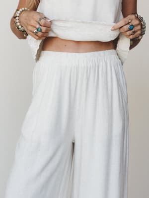 A close-up mid-shot of wide-leg linen pants with an elastic waistband, styled with a cropped top and layered silver and turquoise boho jewelry — soft, relaxed, and effortlessly intentional.