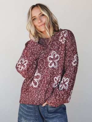 A cozy, oversized knit sweater in marled burgundy with cream daisy appliqués styled with lived-in denim — the kind of sweater that makes a Tuesday feel intentional.