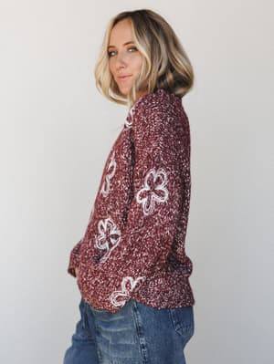 A marled burgundy knit sweater with chunky cream floral appliqués styled with medium-wash straight jeans — the kind of sweater you reach for every weekend without thinking twice.
