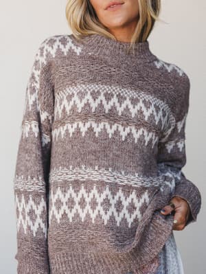 A cozy Fair Isle knit sweater in warm mocha and cream photographed close on a model — the kind of sweater that makes you want to pour something hot and not go anywhere.