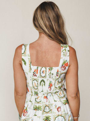 Shot from behind, a model wears an ivory sleeveless top with a detailed tropical toile print — smocked back bodice, wide square straps, and a tiered hem give it that effortless warm-weather feel.