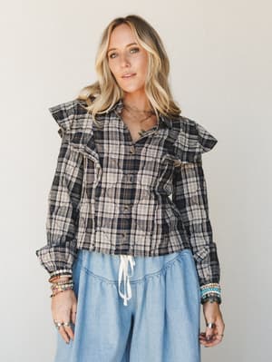 A quilted plaid ruffle blouse in navy and cream styled with wide-leg chambray pants and stacked beaded bracelets — the kind of outfit that feels put-together without trying too hard.