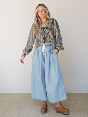A gingham ruffle blouse tucked into breezy wide-leg chambray pants, styled with wood-studded clogs and stacked jewelry — the kind of outfit that looks intentional without trying too hard.