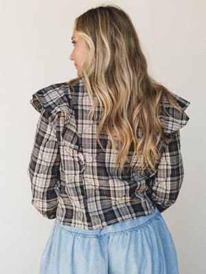Shot from behind, a model in a navy plaid quilted blouse with dramatic ruffle shoulder trim is paired with a soft blue tiered skirt — the kind of outfit that feels intentional without trying too hard.