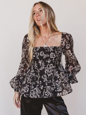 Woman wearing a black floral blouse against a plain background