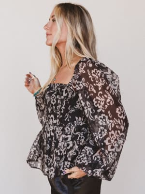 Woman wearing a black floral blouse against a plain background