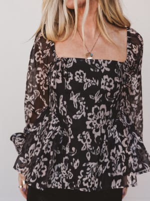 Woman wearing a black floral blouse against a plain background