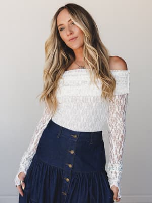 A lace off-shoulder bodysuit in cream pairs with a dark denim button-front skirt for a mix that feels equally romantic and grounded — the kind of outfit that works harder than it looks.