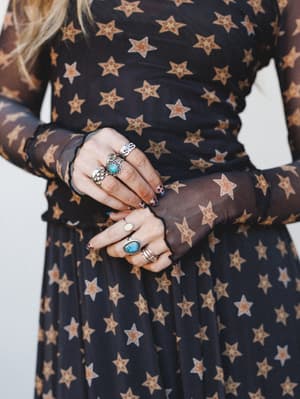 A close-up of layered silver rings and turquoise stones resting against the waist of a sheer mesh long-sleeve dress covered in warm golden star print — the kind of detail shot that makes you want to raid someone's jewelry box.