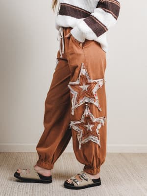 Brown pants with star patterns worn by a person on a neutral background