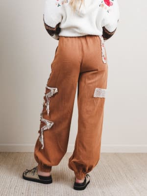 Brown pants with lace patches worn by a person against a plain background