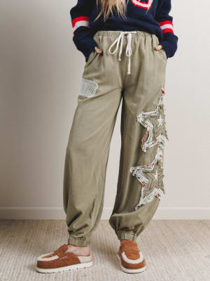 Person wearing olive green pants with decorative elements and a navy sweater with red and white accents.