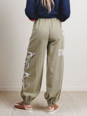Person wearing olive green pants with lace patches on a plain background