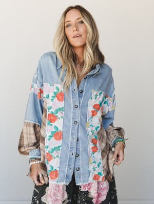 A patchwork denim shacket layered with floral and plaid fabric panels worn open over a dark floral skirt — the kind of piece that looks like it was assembled from your most-loved vintage finds.