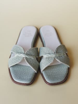 A pair of mint woven raffia slide sandals shot flat from above, with crossover straps and a delicate braided accent detail — the kind of shoes that make you want to book a flight somewhere warm.