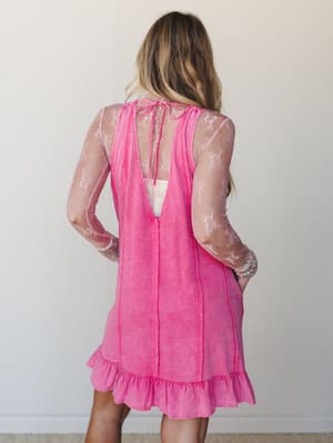 A back-view shot of a layered mini dress look — a washed fuchsia sleeveless dress with an open tie-back and ruffle hem worn over a sheer pink floral mesh long-sleeve top, giving it that effortless, throw-it-together energy that actually took some tho