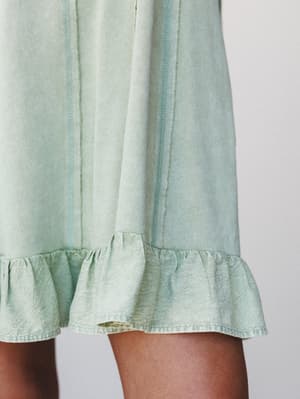 A close-up detail shot of a soft mint dress hem, showing the contrast between a ribbed knit body with exposed seaming and a crinkled satin ruffle trim — the kind of thoughtful mixed-fabric detail that makes a simple dress feel a little special.