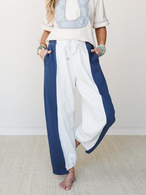 Wide-leg colorblock pants in grey and navy with a drawstring waist, styled with an embroidered cream top and stacked beaded bracelets — relaxed and expressive with an easy, lived-in feel.