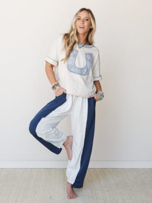 A relaxed, full-body shot of a model in a cream graphic tee and wide-leg color-block pants — cream with navy side panels — styled with stacked turquoise and beaded bracelets for an effortlessly put-together, cozy-cool vibe.
